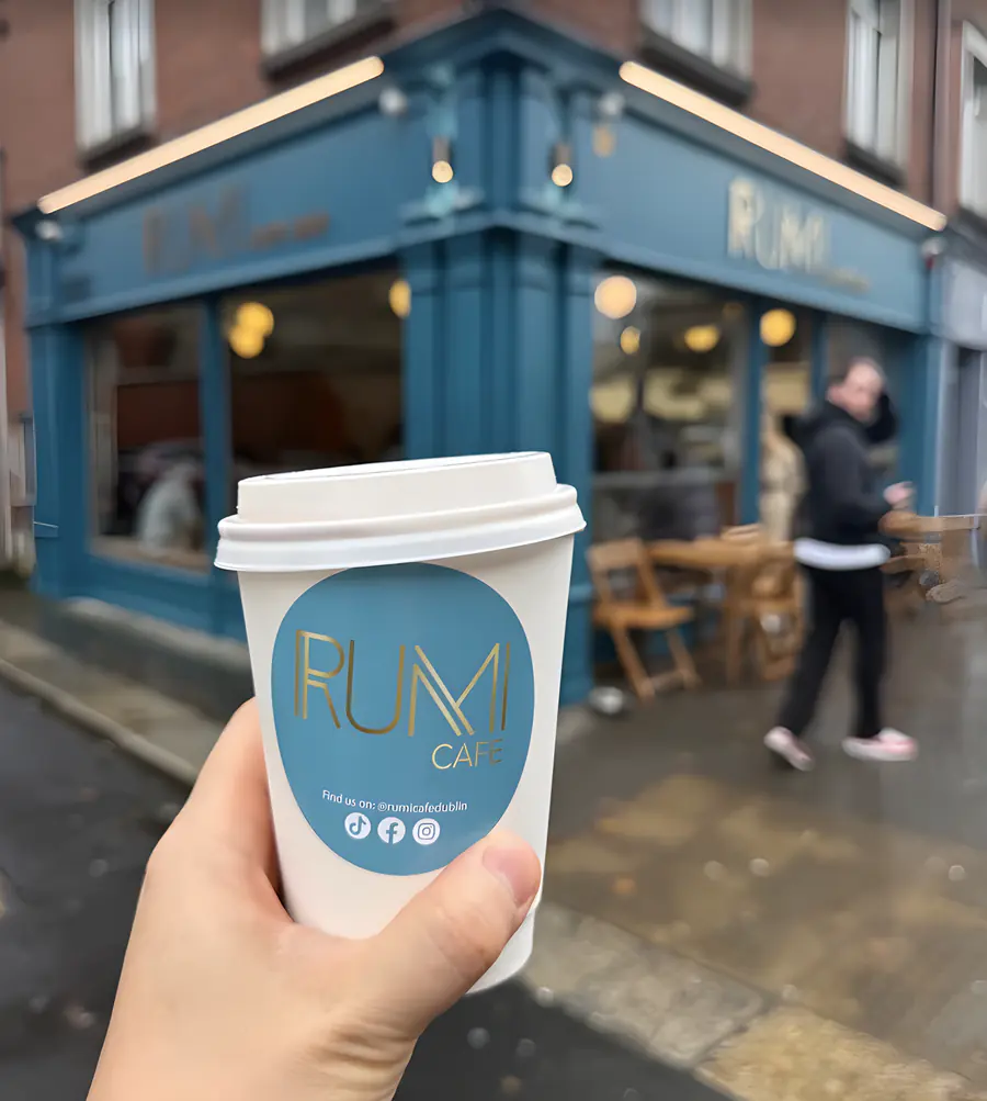 A takeaway cup with the Rumi logo outside the café